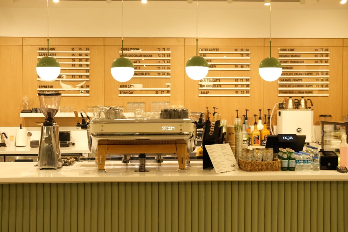 A cafe service counter with printed menu boards behind the espresso machine