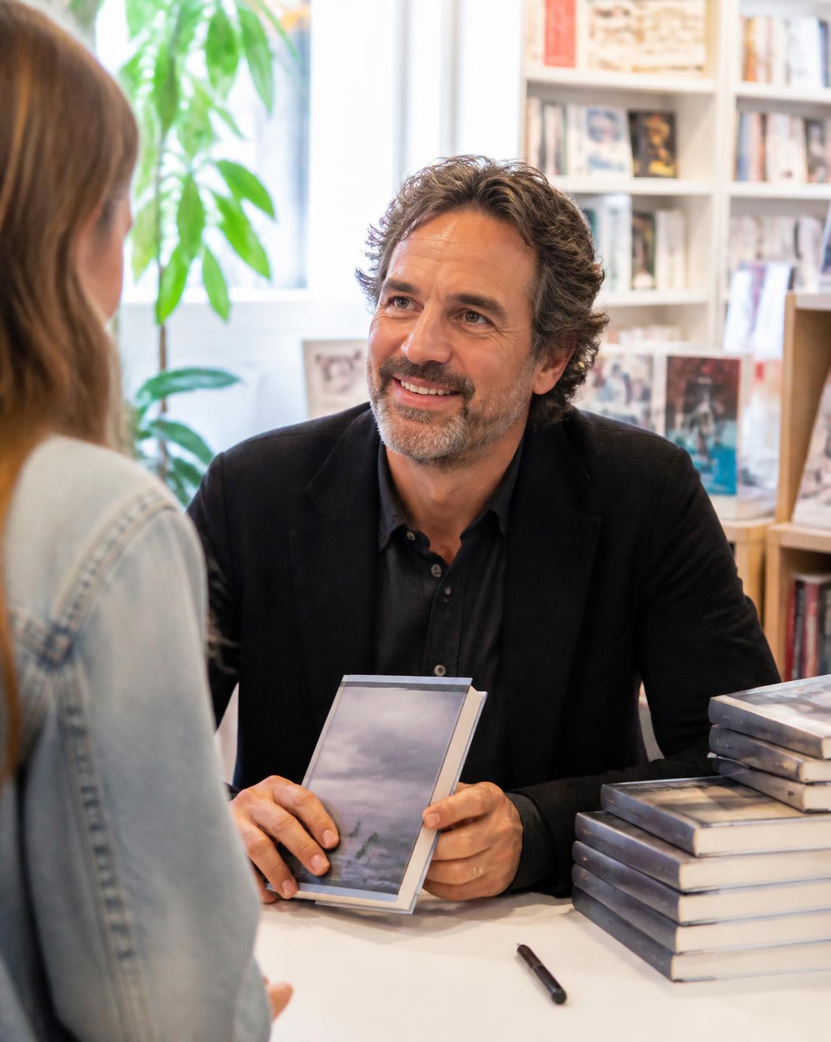 An author signing copies of his book for a reader in a bright bookshop