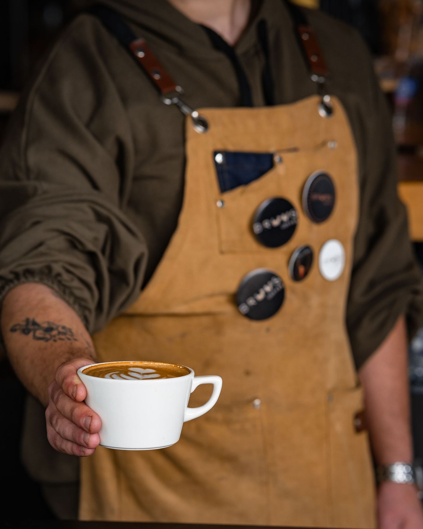 A barista wearing a leather work apron holding a coffee